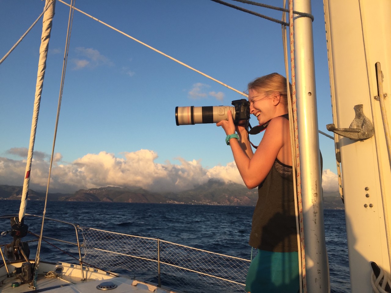 A person with long blonde hair using a telephoto lens camera on a ship in the ocean.