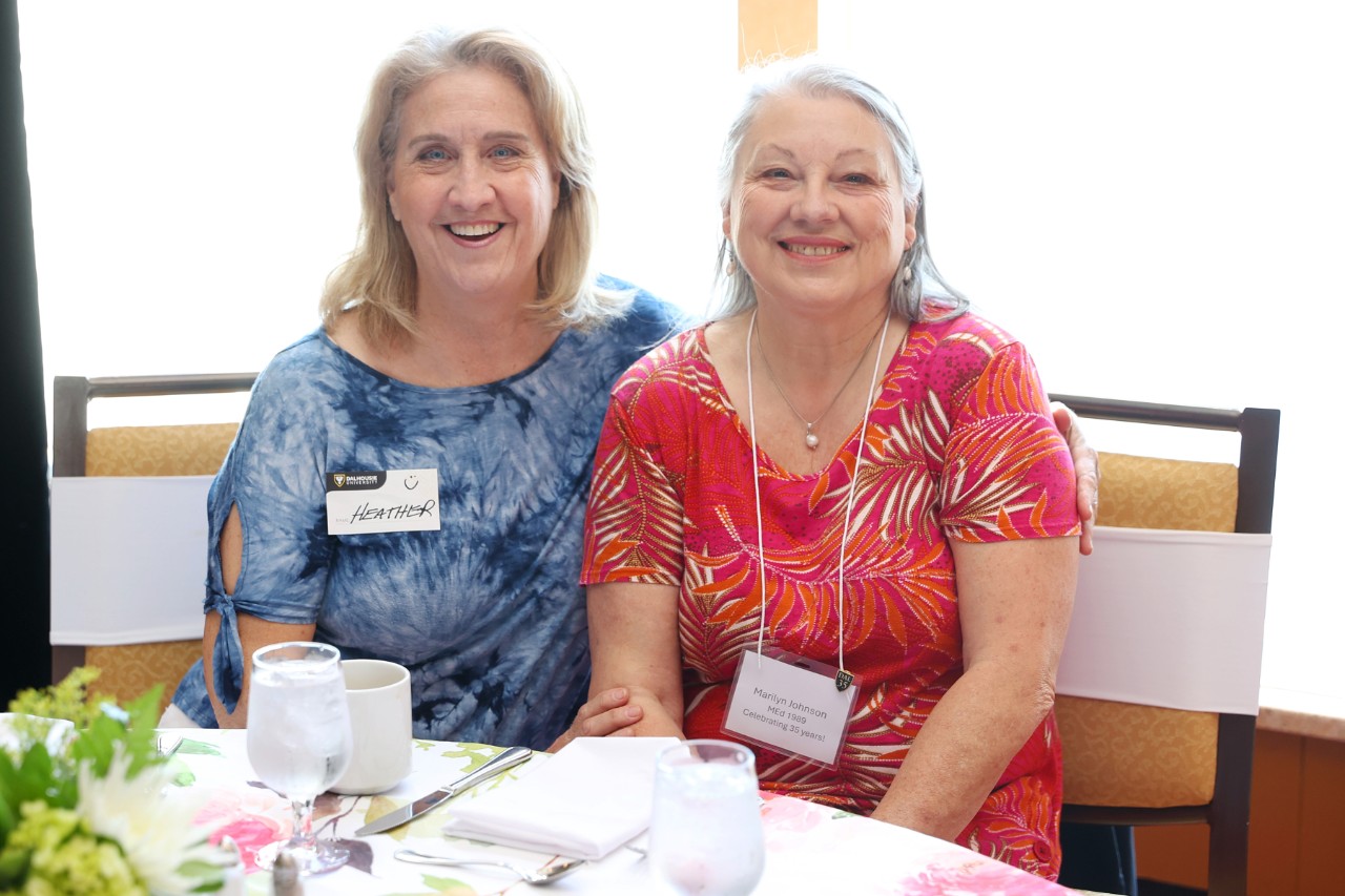Two women are seated at a table close together smiling.