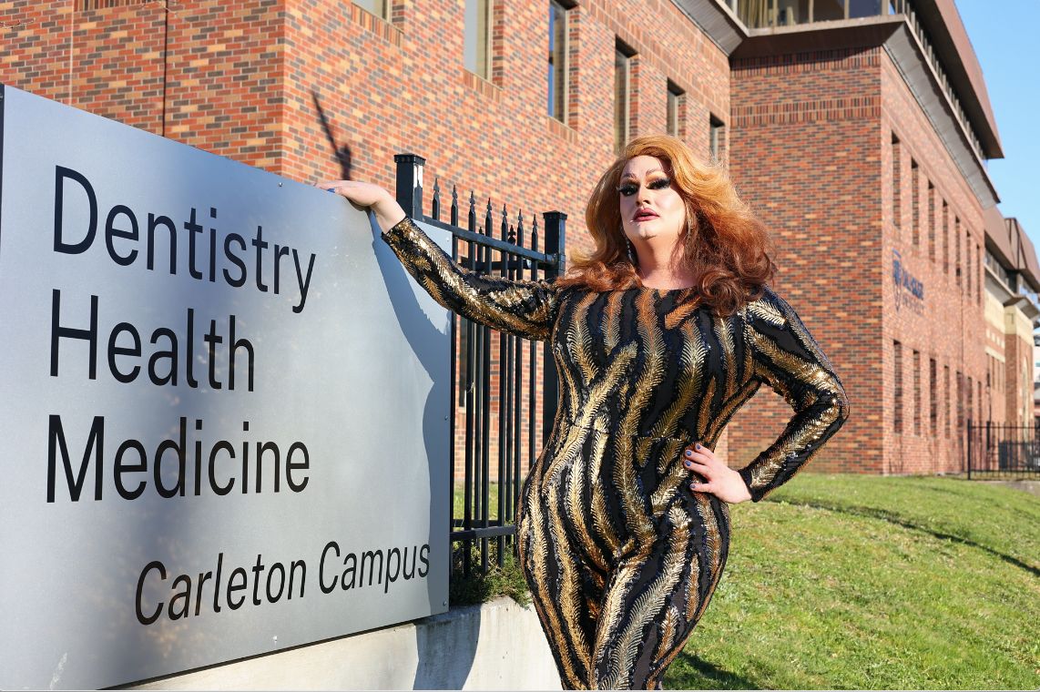 Pelrine as Bunni Lapin is standing outside of a building in front of the Carleton Campus sign.