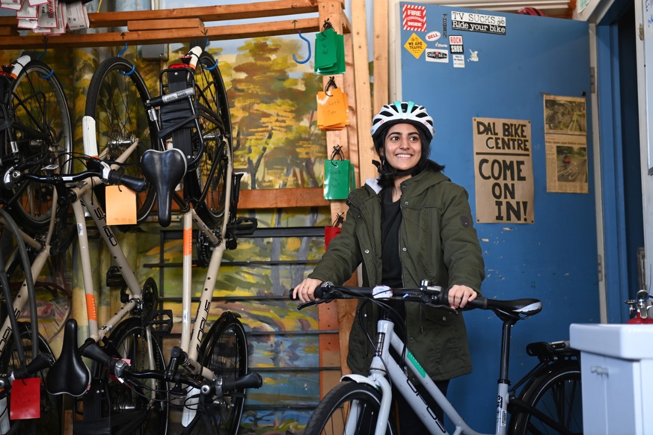 A student wearing a helmet smiles next to a white bicycle outside the Dal Bike Centre.