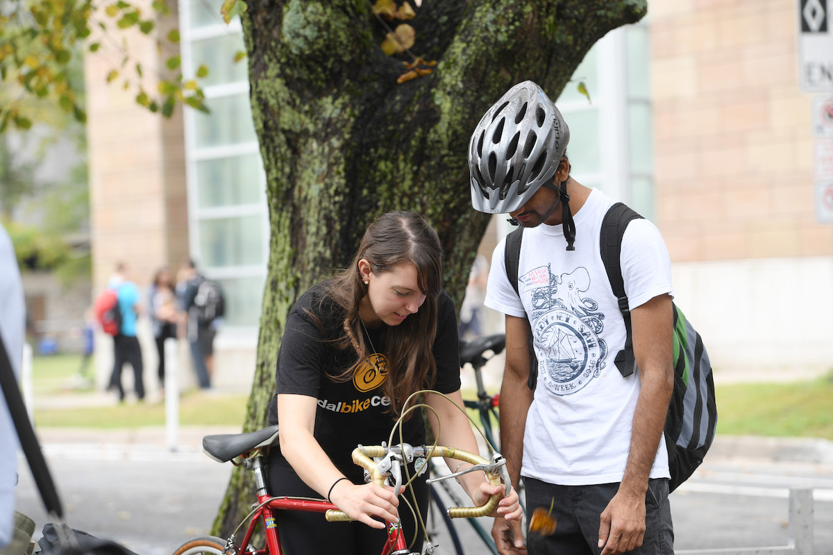 One cyclist checks brakes on bike while second cyclist looks on.