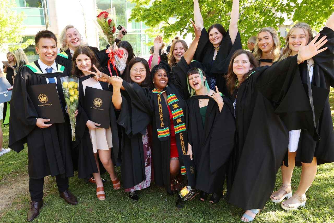 A dozen students are wearing their graduation gowns with their arms up in the air in celebration. 