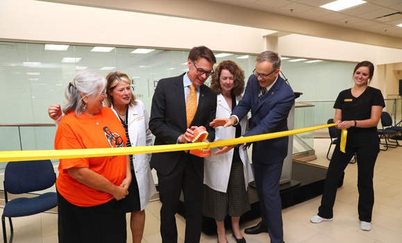 Group of individuals cutting a yellow ribbon.