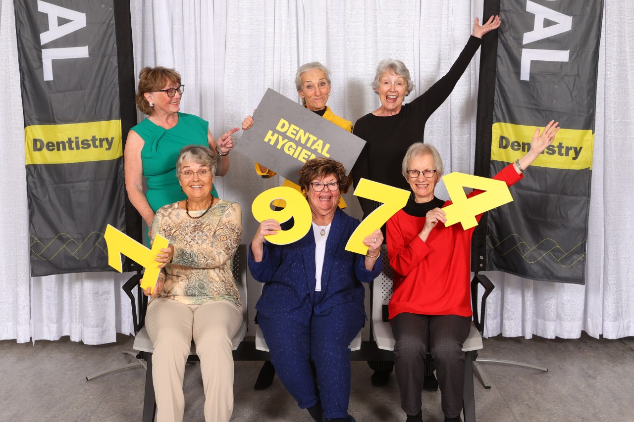 Six women pose together at an event with "1974" number signs.