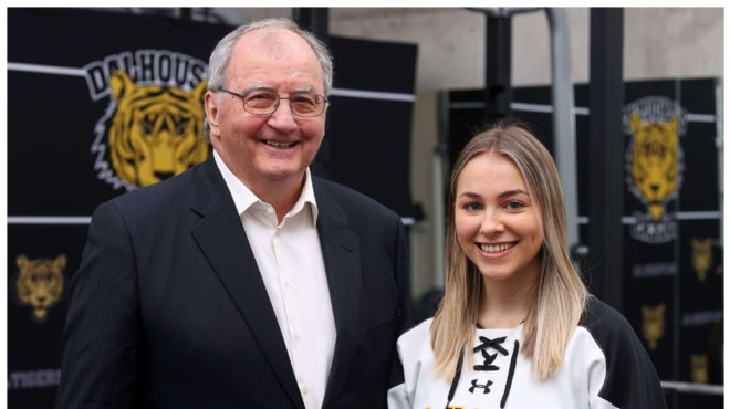 A man in a suit standing with a young woman wearing a hockey jersey
