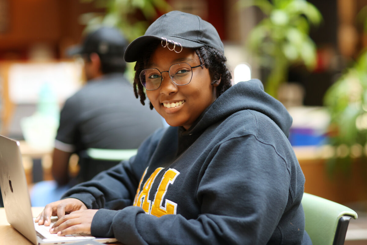 A person with a ball cap and Dal branded sweater at a computer.