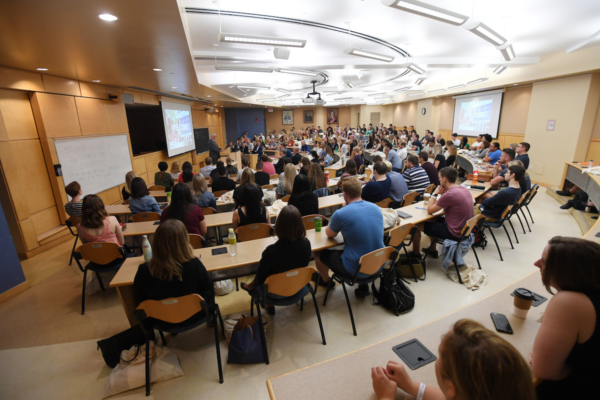 A half moon classroom is full of students, faculty and staff.