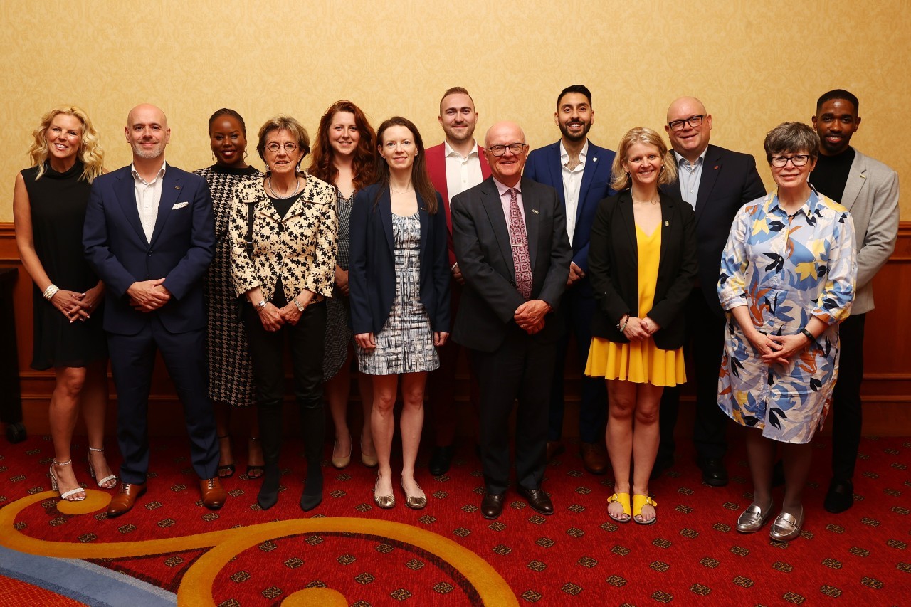 A group of men and women pose in semi-formal attire at an event.