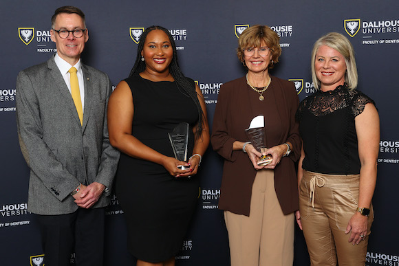 Faculty and alumni members stand together at an event with two holding awards. 