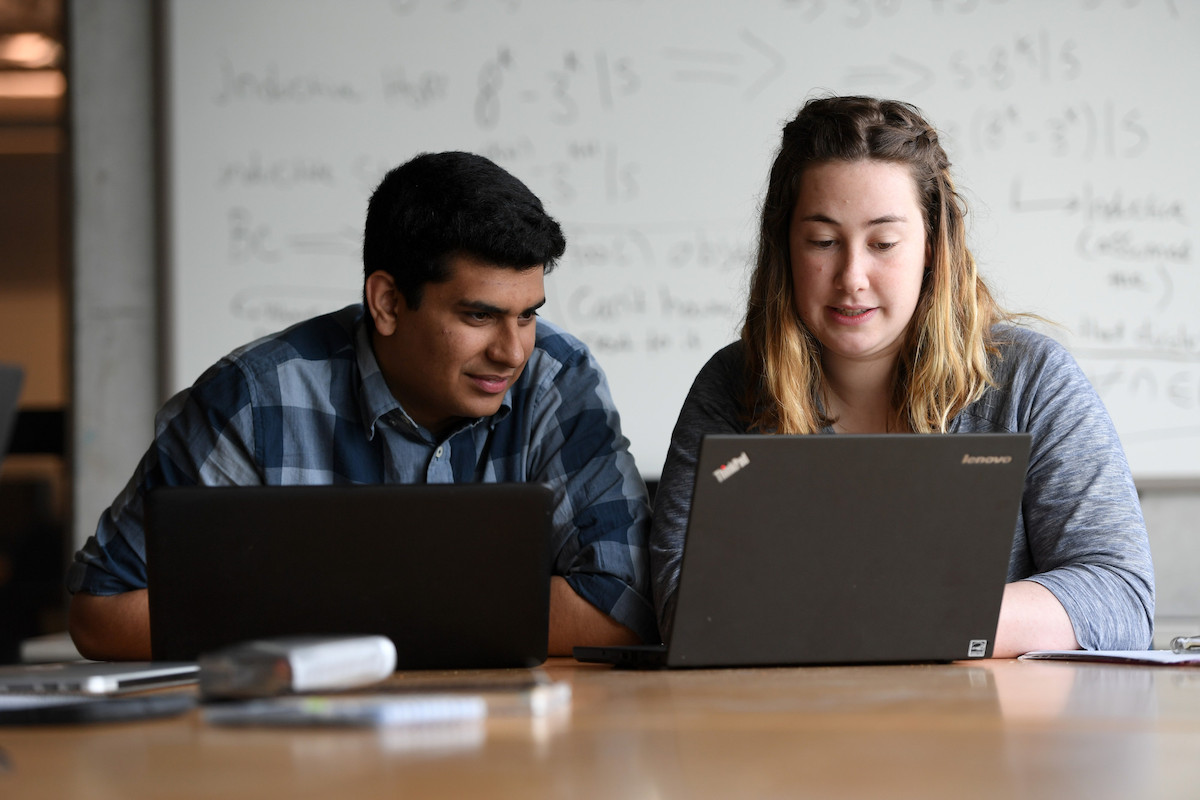 Two students sitting at desk using laptops. 