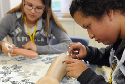 Two people practice stitching on a plastic arm