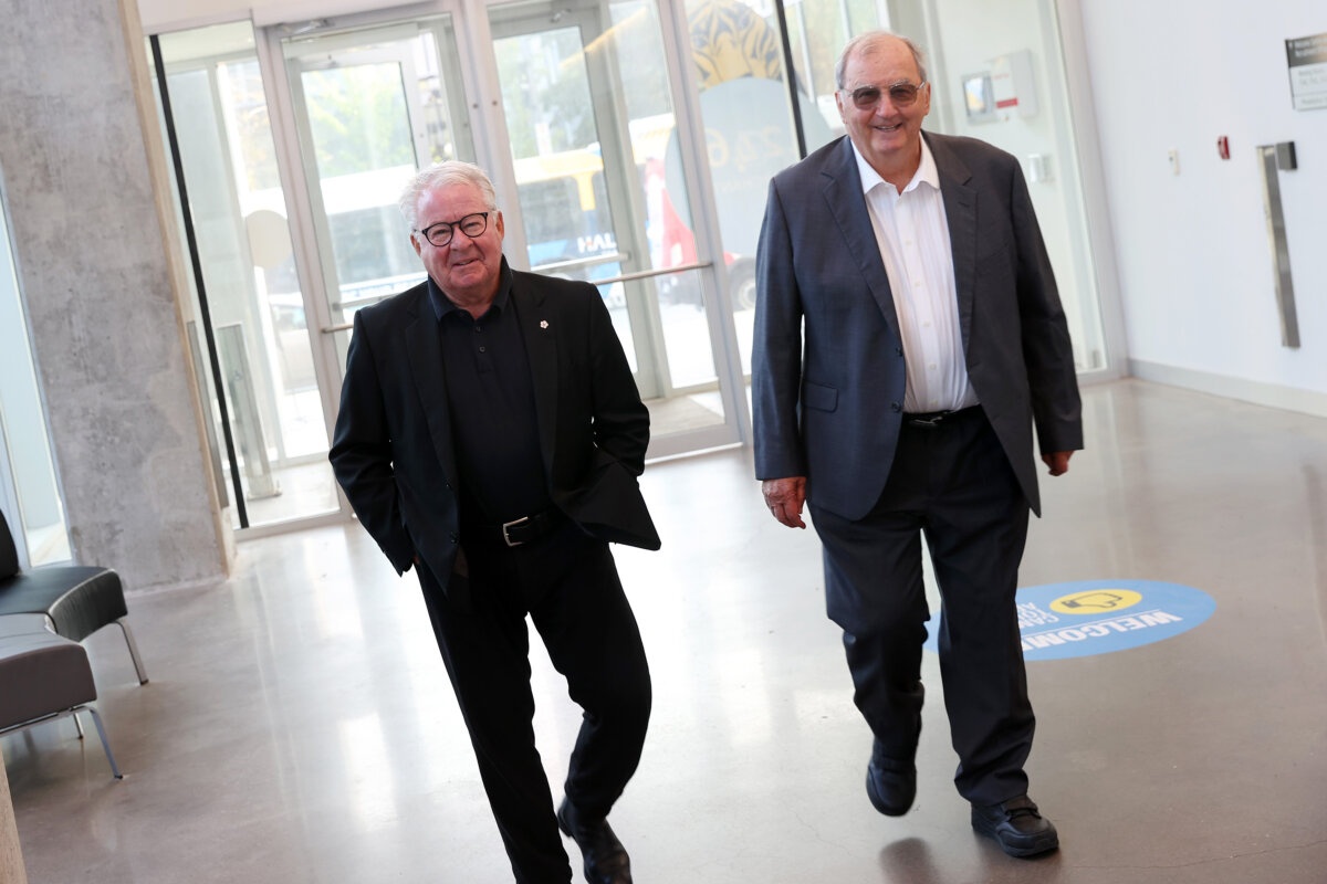 Two men wearing suits walk down a hall