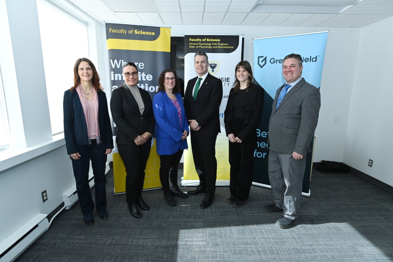 A group of men and women wearing suits stand in front of three pop up banners