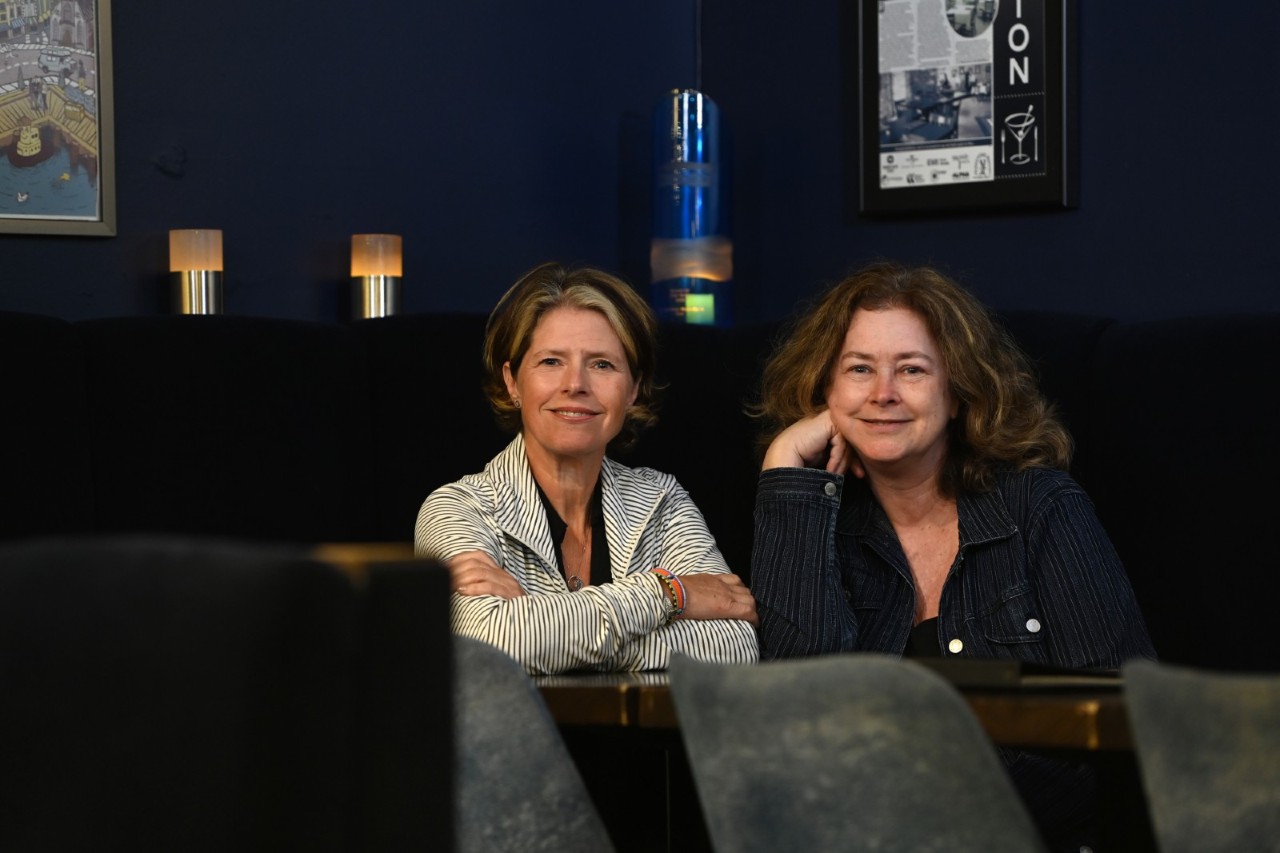 Lisa Murphy and Karen Spaulding leaning against a bar top in a restaurant, smiling.