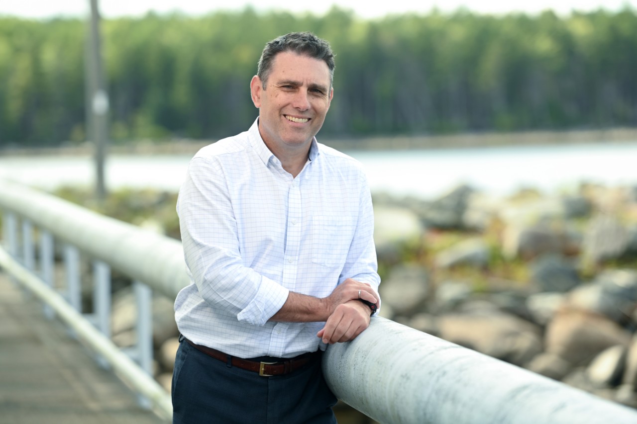 Portrait of a man dressed in business casual leaning against the rail of a bridge on a coastal trail.