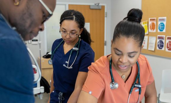 Three health practitioners wearing scrubs work together in a clinic.