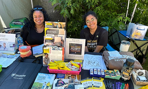 Two individuals sit at a table covered with pamphlets and Dal swag.