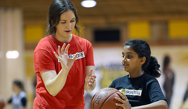 photo of female student showing young female how to play basketball