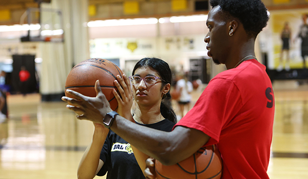 A male student coaches a female student holding a basketball, getting ready to take a shot.