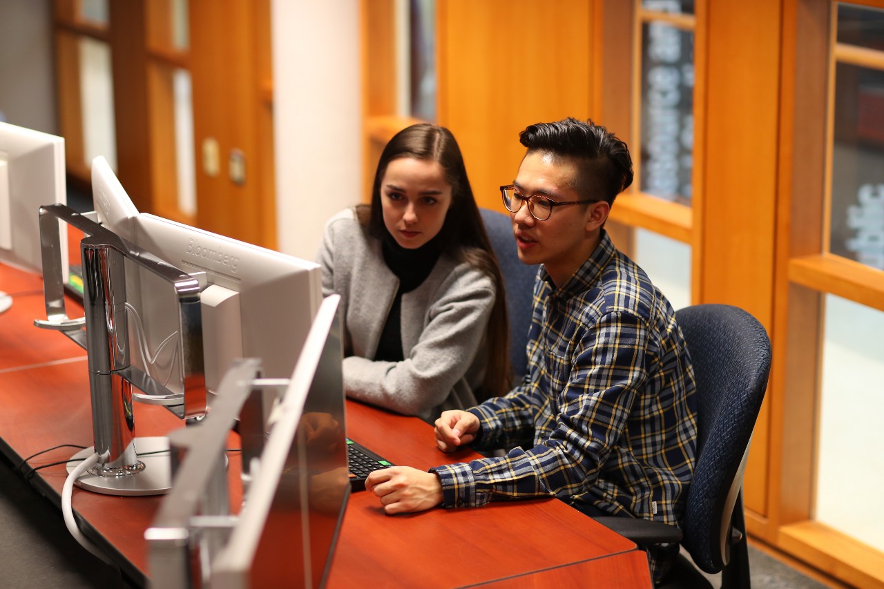 A woman and a man seated at a desk looking at a computer screen