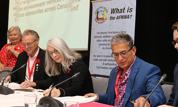 Four individuals signing documents, with an Atlantic First Nations Water Authority (AFNWA) banner in the background.