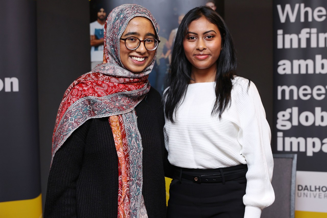Two female-presenting students of diversity smiling at an event for Women in STEM.