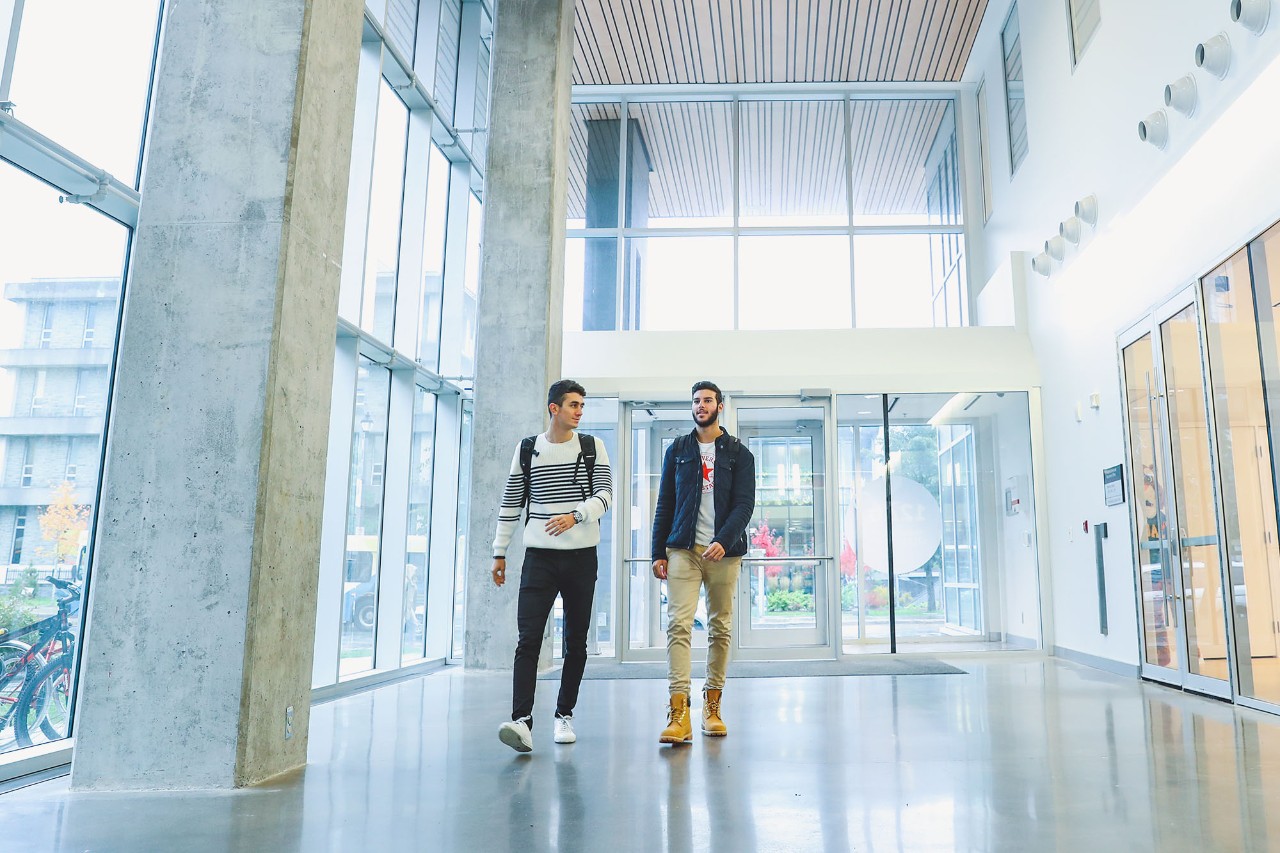 Two students walking along the brightly lit, windowed hall near the entrance of Dal's Health and Wellness Centre.