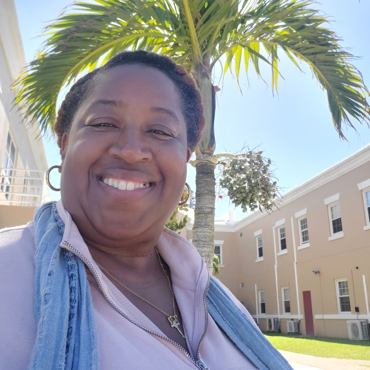 James-Outerbridge smiling in the sunny outdoors with a palm tree in the background.