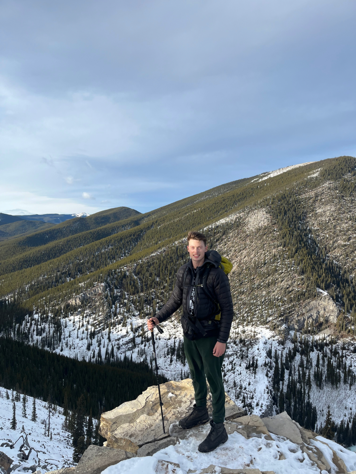 William Mai standing atop a mountain with some snow cover in hiking gear in Alberta.