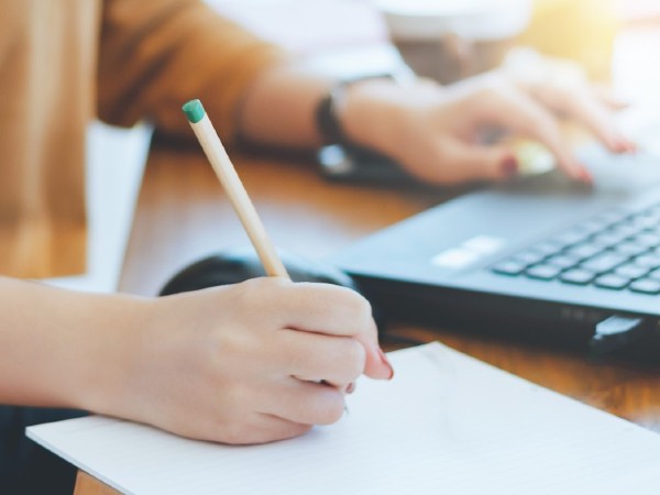 A person writes on a notebook and types on a laptop