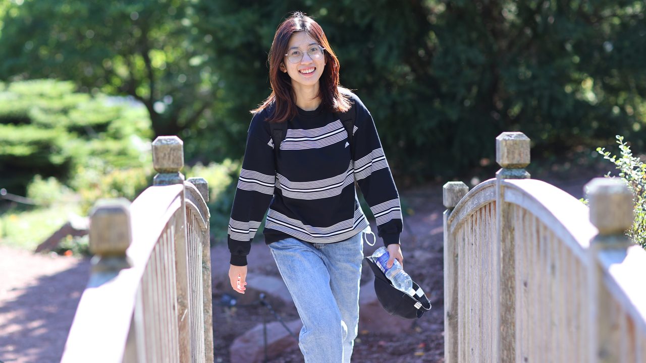 Student walking on wooden footbridge smiling.