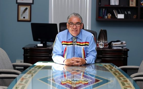 Chief Sidney Peters sits at a table in his office with his hands clasped and smiling.