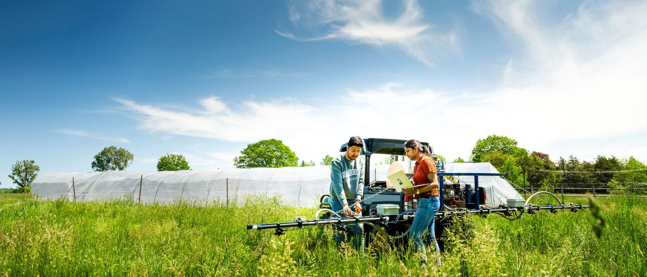 Two students in a green field working on a tractor. 