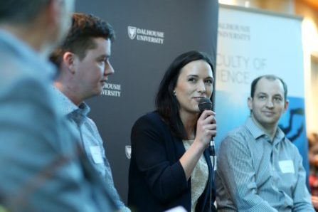 Focus on a woman speaking into a microphone seated between three others at a panel event. 