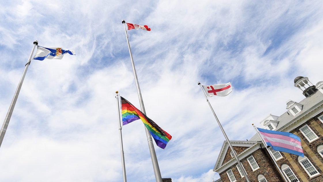 The Nova Scotia, Canadian, Mi'kmaq, pride, and trans flags flying on the Studley Quad. The MacDonald Building can be viewed in the backgroudn.