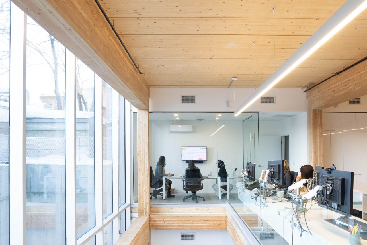 View from the second story of an open concept office space with wood ceilings and beams while people are at work.
