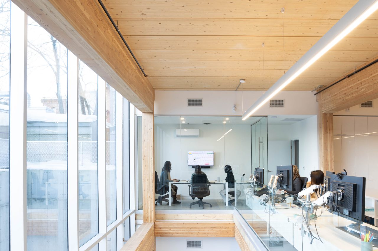 View from the second story of an open concept office space with wood ceilings and beams while people are at work.