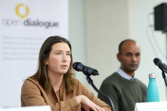 A woman sitting in front of a microphone with a man seated to the right in front of a microphone