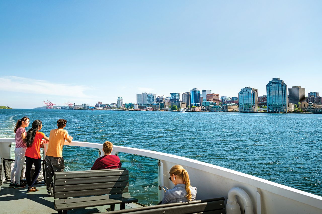 A group of 3 students on the top deck of the ferry with Halifax skyline in the distance.