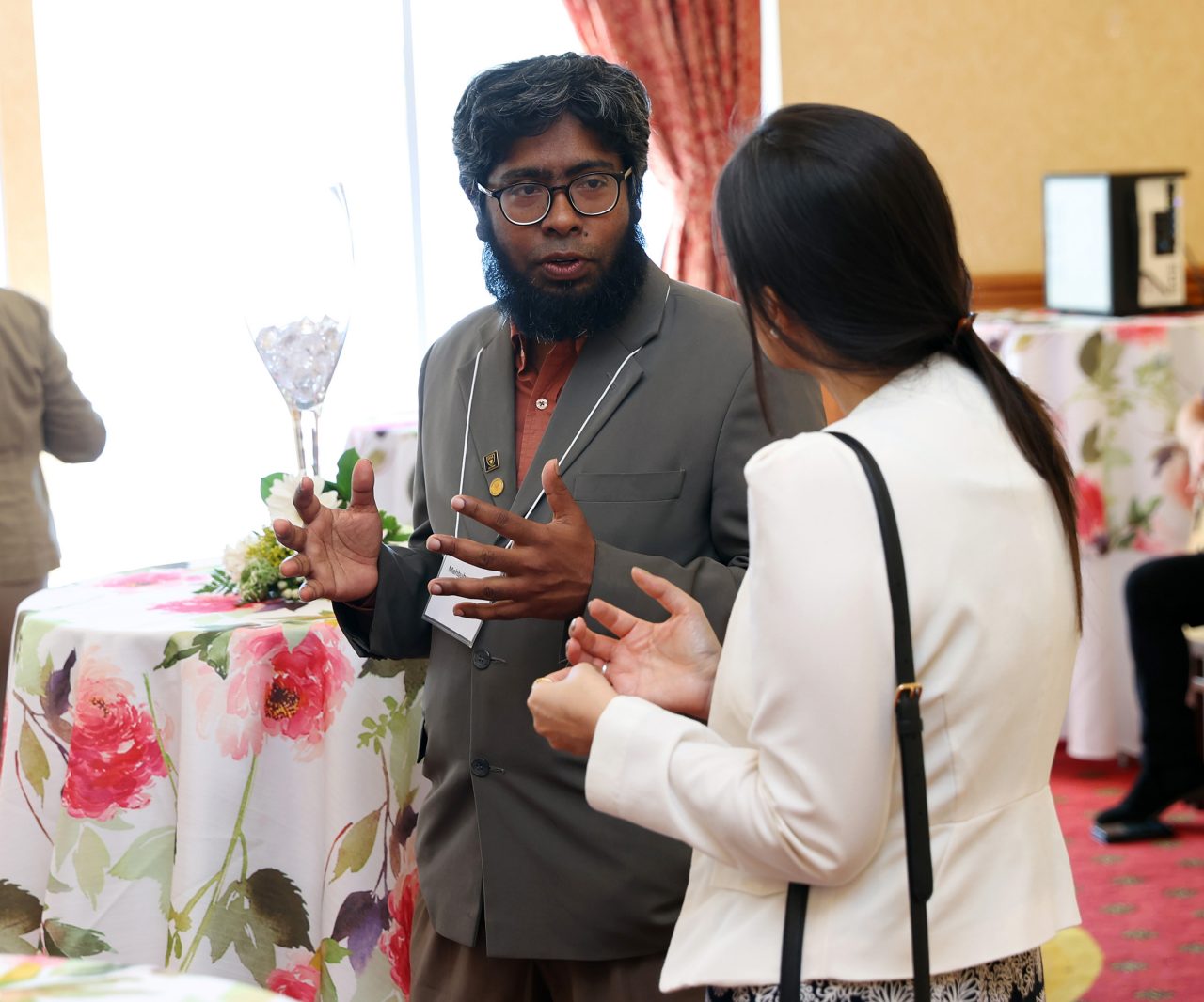 Rahman is standing and in conversation with a woman at the Champagne Social event.