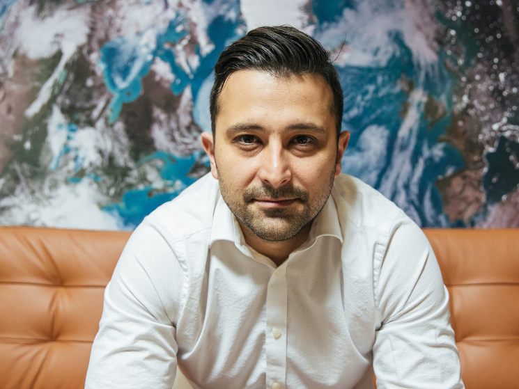 Engineer Arad Gharagozli sits on a couch in front of a wall with a large image of planet Earth.