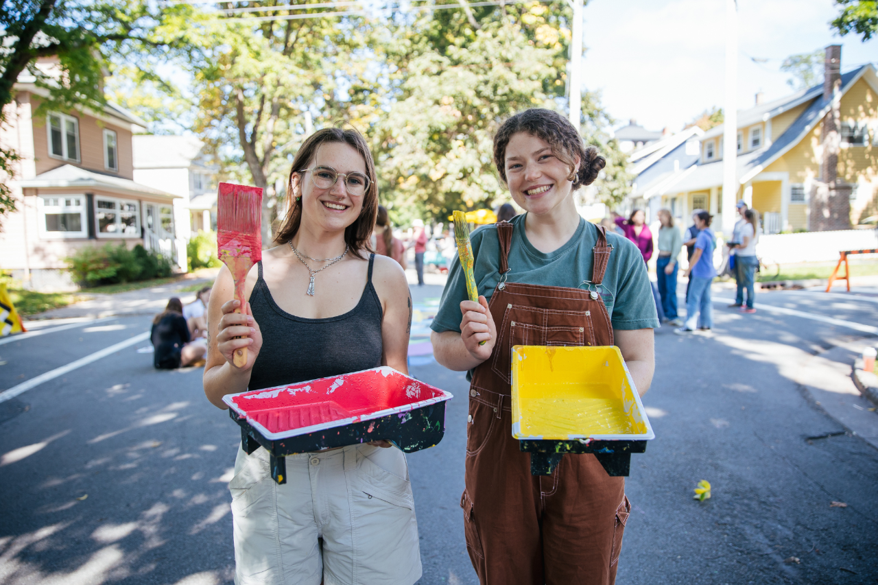 two female students holding paint trays and paint brushes
