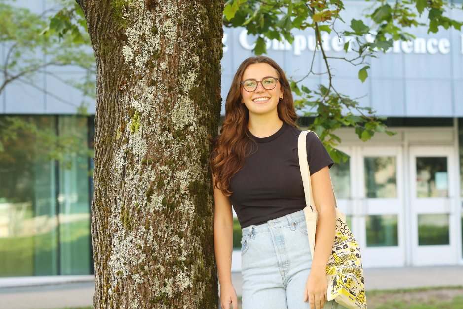 Woman standing beside tree outside of campus building.