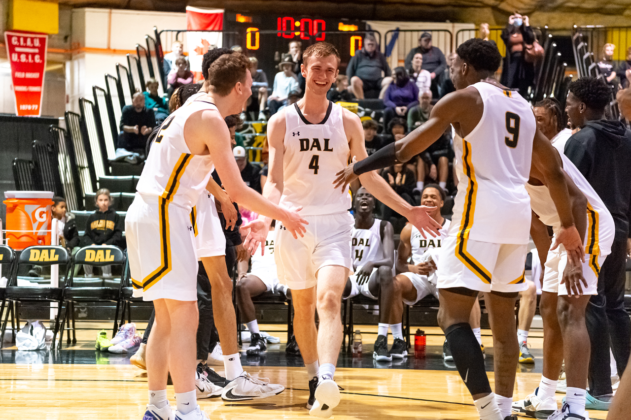 A player in a white jersey runs to high-five two other players in white jerseys on a basketball court