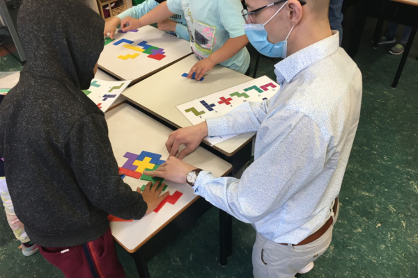 A person wearing a mask kneeling at  table to help a child with a puzzle