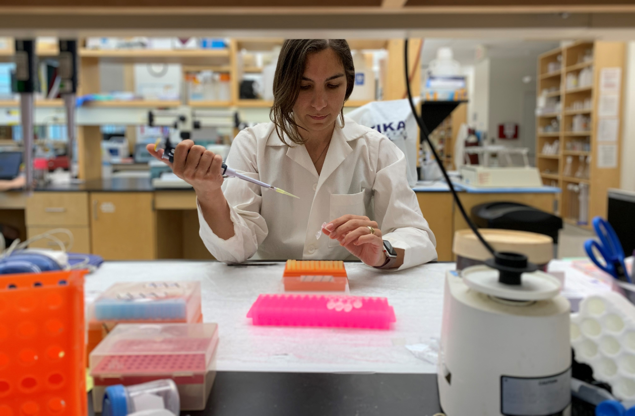 A scientist in a lab coat working with a pipette in a laboratory setting.